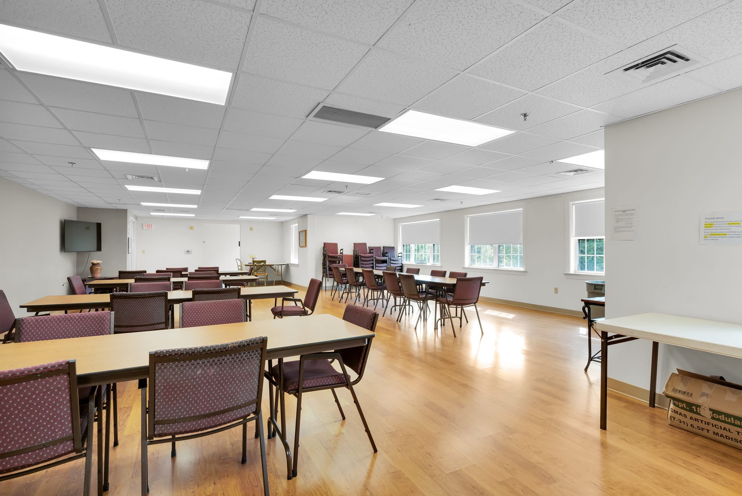 The community dining room, with long tables and chairs under tall windows