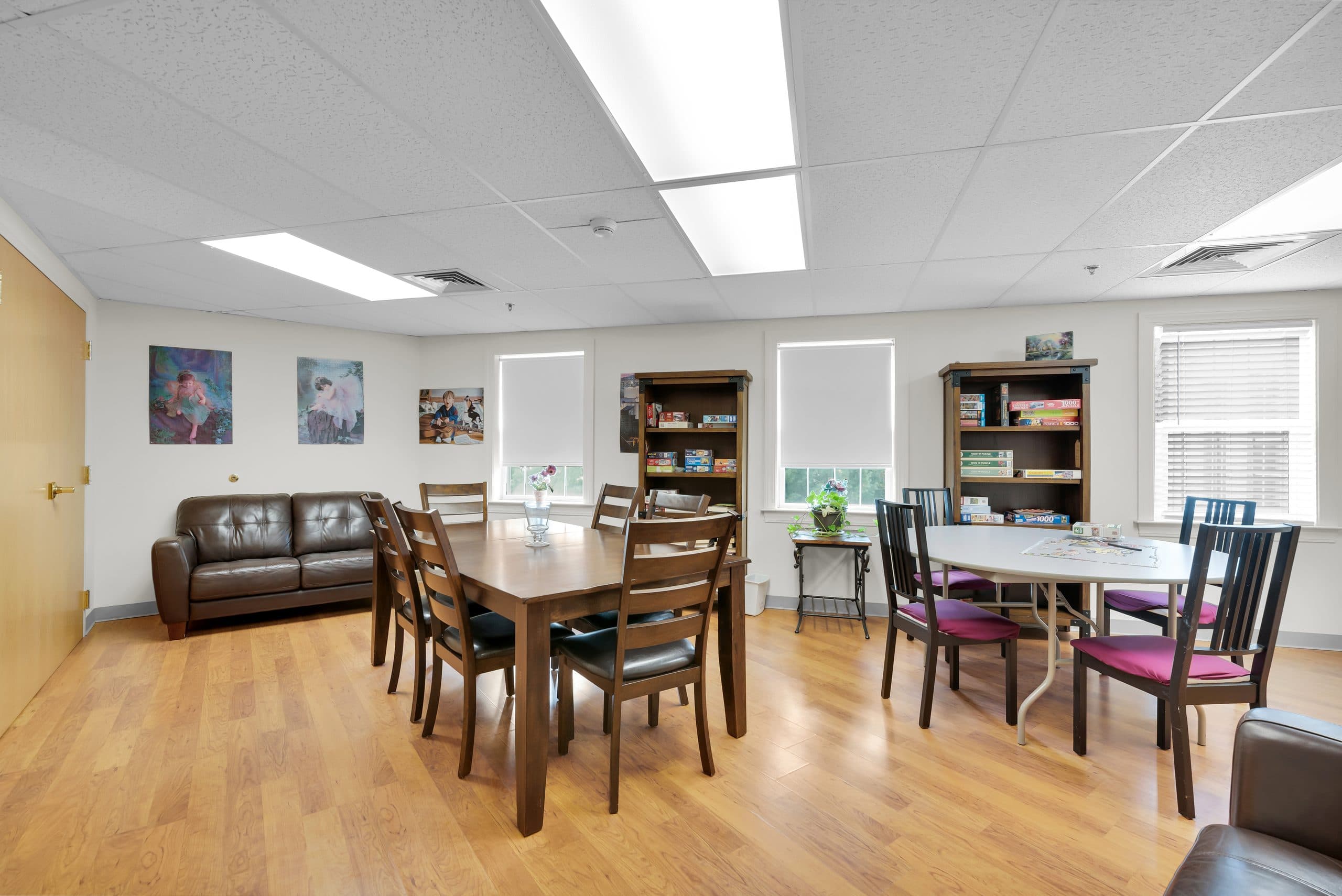 The library lounge — bookcases, a leather sofa, and dining tables for cards and puzzles
